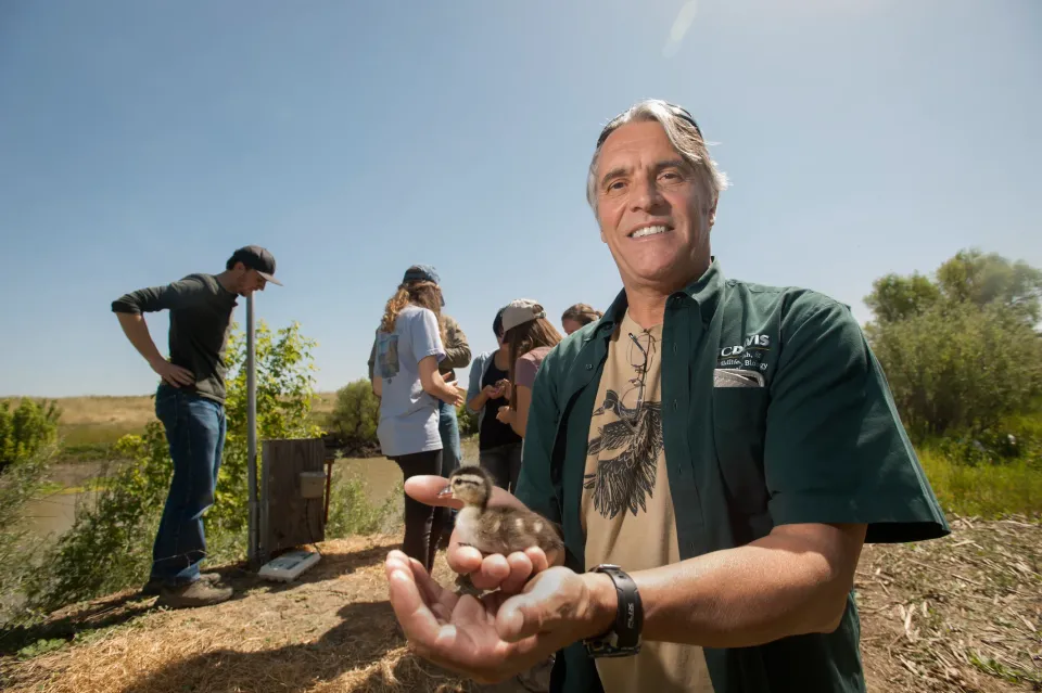 Professor John Eadie holds duckling with students in background outside