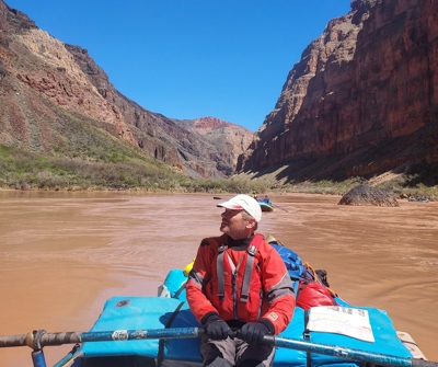 Nicholas Pinter rows a boat on the water with a red rock vista in the background.