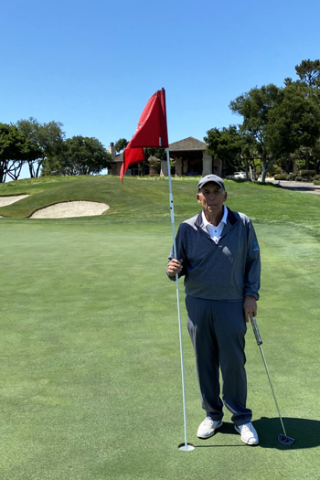 Donor Bill Owens poses with a golf club while holding onto the flag at a hole in a golf course.